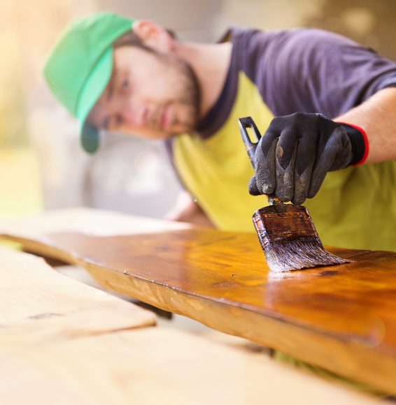 Handyman varnishing pine wooden planks in patio outside the new house